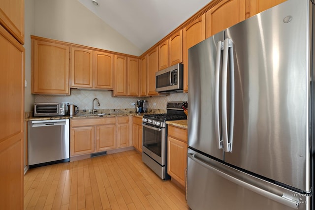 kitchen featuring stainless steel appliances, vaulted ceiling, a sink, light stone countertops, and backsplash