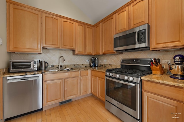 kitchen featuring stainless steel appliances, a sink, light stone counters, lofted ceiling, and backsplash