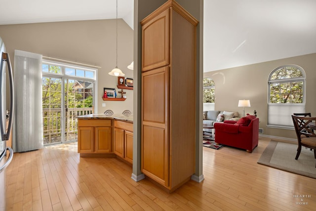 kitchen with high vaulted ceiling, light wood-style floors, healthy amount of natural light, and light stone countertops