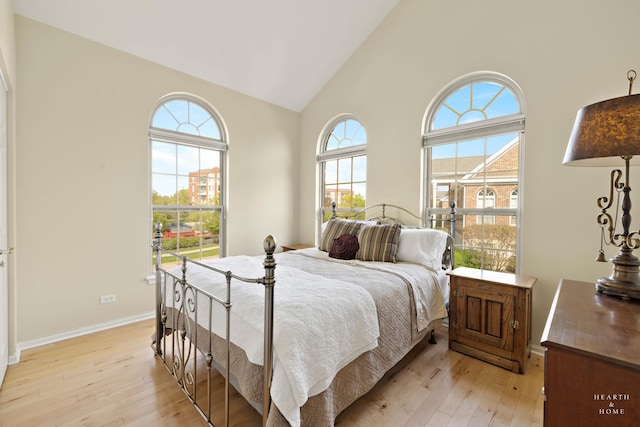 bedroom featuring light wood-style floors, high vaulted ceiling, and baseboards