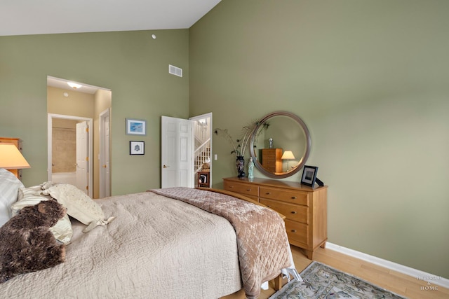bedroom featuring high vaulted ceiling, light wood-type flooring, connected bathroom, and baseboards