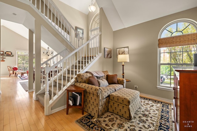 living area featuring high vaulted ceiling, plenty of natural light, stairway, wood finished floors, and a chandelier