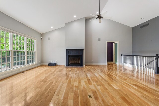 unfurnished living room featuring light wood finished floors, high vaulted ceiling, a ceiling fan, a fireplace with flush hearth, and baseboards