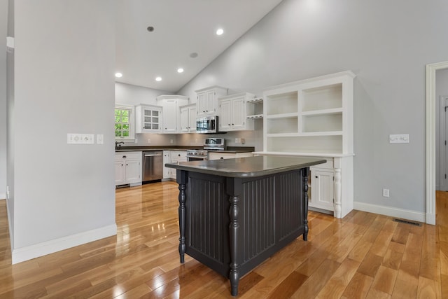 kitchen with appliances with stainless steel finishes, open shelves, dark countertops, white cabinetry, and light wood-style flooring