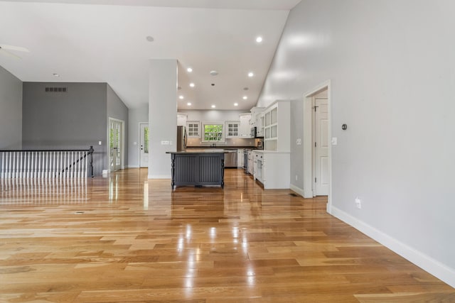 unfurnished living room with light wood finished floors, high vaulted ceiling, ceiling fan, baseboards, and recessed lighting