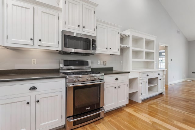 kitchen featuring open shelves, stainless steel appliances, dark countertops, light wood-style floors, and vaulted ceiling