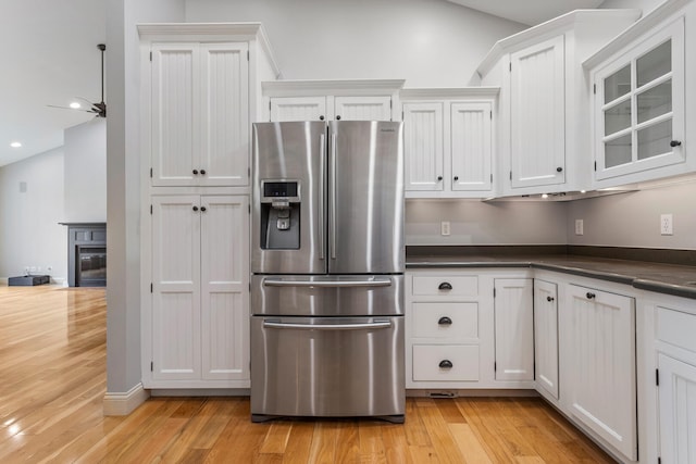 kitchen with stainless steel fridge, light wood-type flooring, dark countertops, white cabinets, and recessed lighting