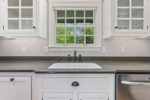 kitchen featuring dishwasher, a sink, dark countertops, and white cabinetry