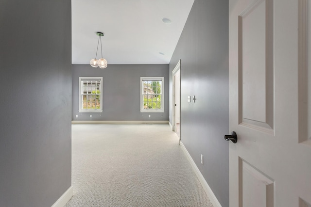 hall with carpet floors, baseboards, lofted ceiling, and a chandelier