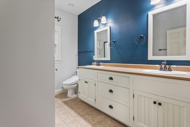 full bath with toilet, tile patterned floors, double vanity, and baseboards