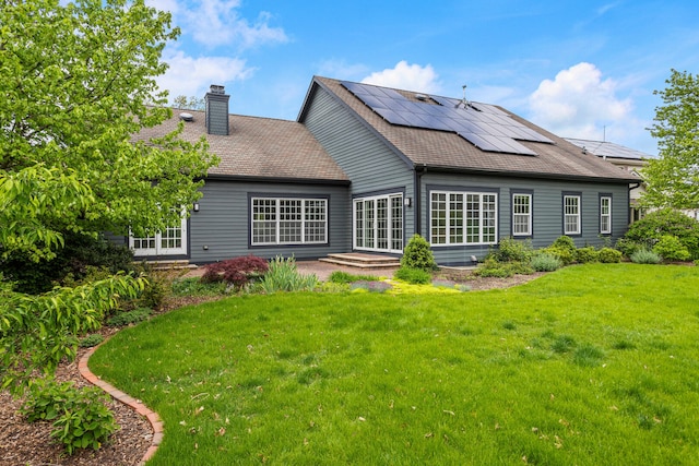 back of property featuring a chimney, a yard, solar panels, french doors, and a patio area