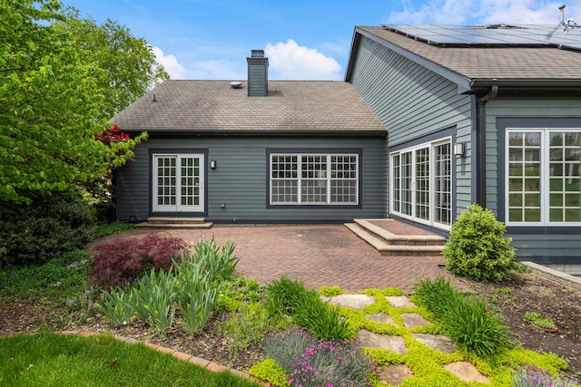 rear view of house with a chimney, a patio, solar panels, french doors, and a shingled roof