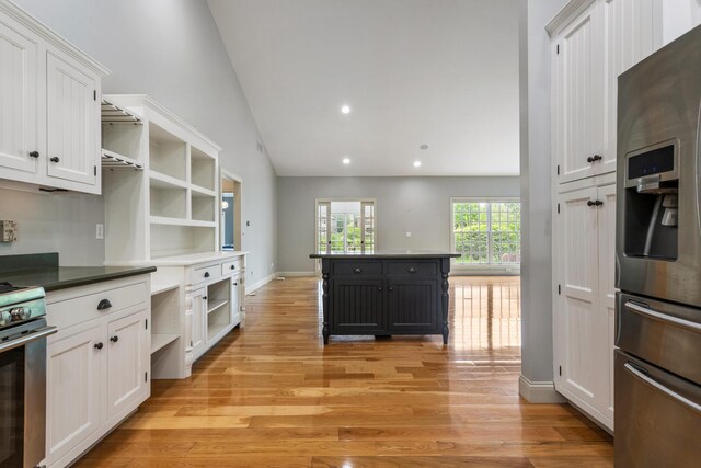 kitchen with stainless steel appliances, open shelves, white cabinets, vaulted ceiling, and light wood-type flooring