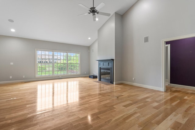 unfurnished living room with high vaulted ceiling, light wood-type flooring, a ceiling fan, baseboards, and a glass covered fireplace