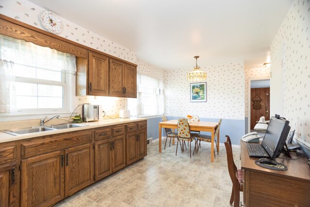 9450 Greenwood Ave, Des Plaines, IL 60016 - kitchen featuring wallpapered walls, a sink, brown cabinetry, light countertops, and decorative light fixtures