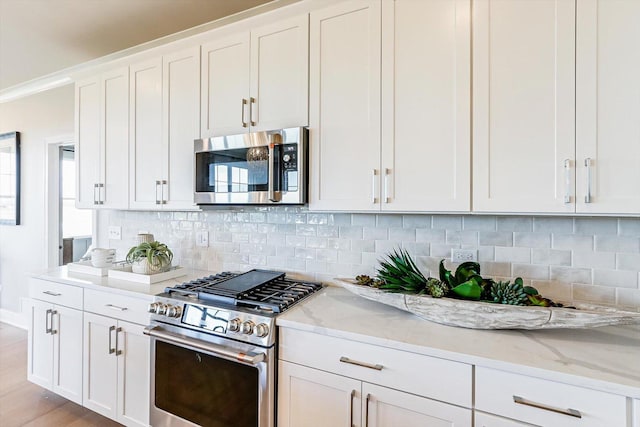 kitchen with white cabinetry, appliances with stainless steel finishes, backsplash, and light stone countertops