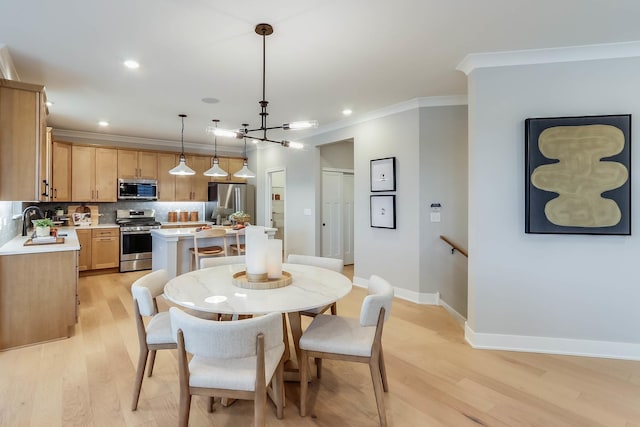dining room featuring baseboards, ornamental molding, light wood finished floors, and a chandelier