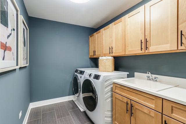 clothes washing area with cabinet space, baseboards, a sink, and washer and clothes dryer