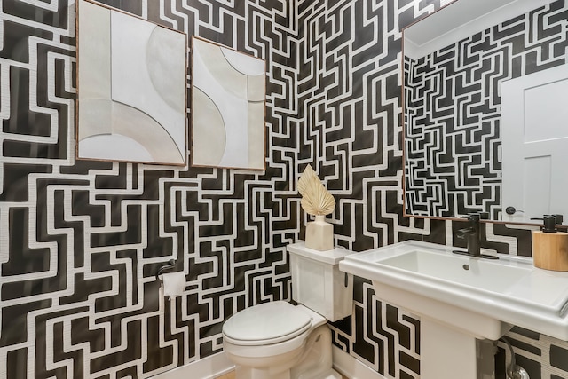 half bathroom with toilet, wallpapered walls, and a sink