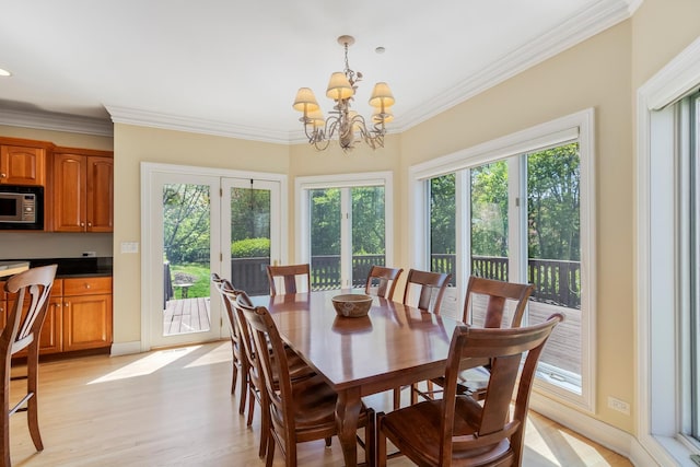 dining space featuring healthy amount of natural light, light wood-style floors, a chandelier, ornamental molding, and baseboards