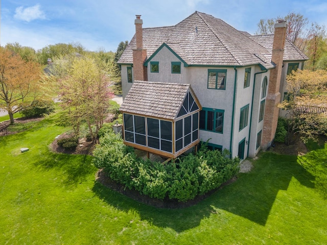 back of property featuring a sunroom, a chimney, stucco siding, and a yard