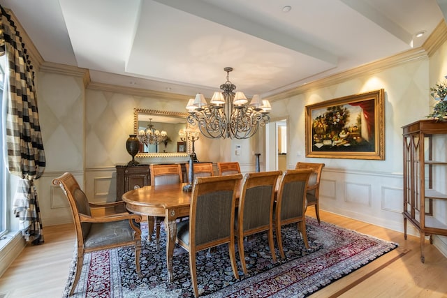 dining area with a decorative wall, a chandelier, light wood-style floors, wainscoting, and ornamental molding