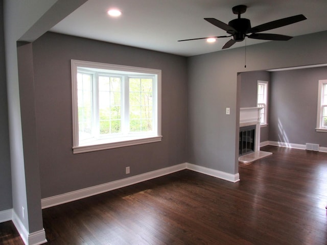 unfurnished room featuring plenty of natural light, dark wood-style flooring, a glass covered fireplace, and recessed lighting
