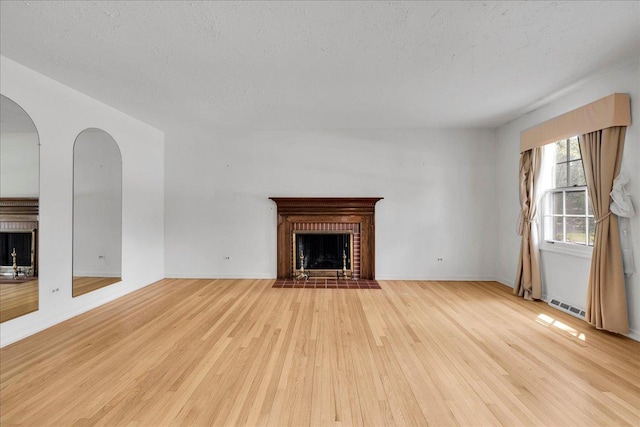 26W266 Tomahawk Dr, Wheaton, IL 60189 - unfurnished living room featuring a brick fireplace, wood finished floors, a textured ceiling, arched walkways, and baseboards