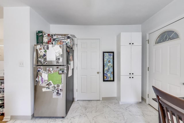 interior space featuring freestanding refrigerator, baseboards, marble finish floor, and white cabinets