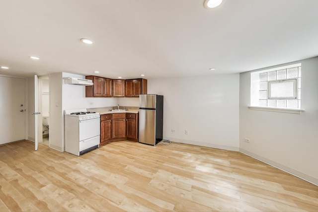kitchen featuring light countertops, a sink, freestanding refrigerator, under cabinet range hood, and gas range gas stove