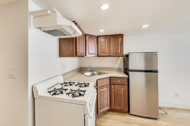 kitchen with freestanding refrigerator, white range with gas stovetop, recessed lighting, range hood, and a sink