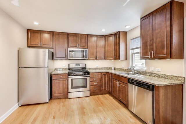 kitchen featuring brown cabinetry, light stone counters, light wood finished floors, a sink, and stainless steel appliances