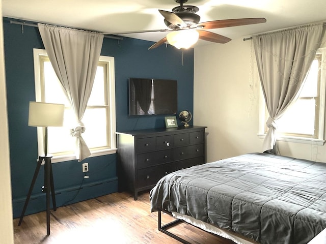 bedroom with baseboard heating, a ceiling fan, and wood finished floors