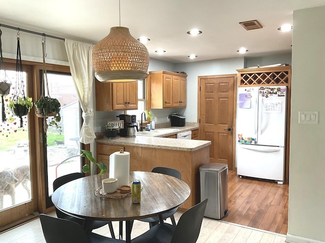 kitchen featuring visible vents, a sink, light wood finished floors, a peninsula, and white appliances