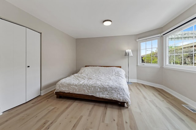 bedroom with visible vents, light wood finished floors, baseboards, and a closet