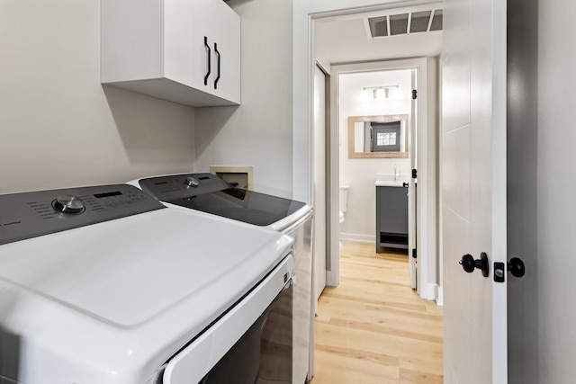 laundry room featuring washer and dryer, light wood-style flooring, cabinet space, and visible vents