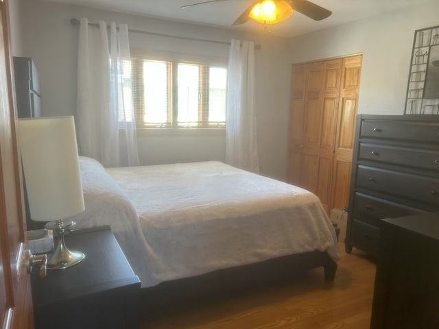 bedroom featuring refrigerator, wood finished floors, a ceiling fan, and a closet