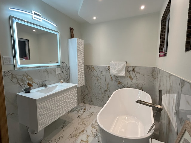 bathroom featuring tile walls, marble tiled flooring, recessed lighting, a soaking tub, and a wainscoted wall