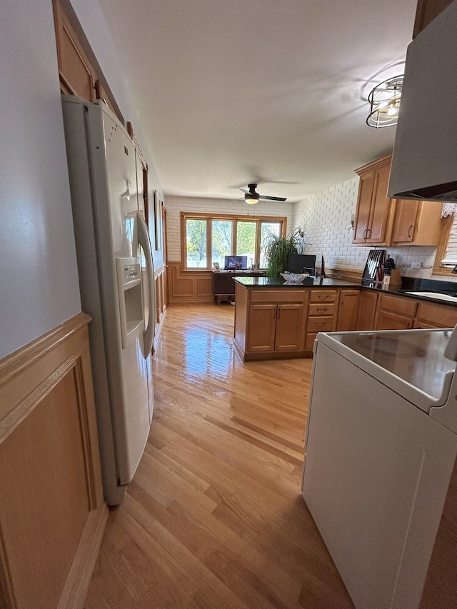kitchen featuring white refrigerator with ice dispenser, light wood-style floors, a peninsula, dark countertops, and a sink