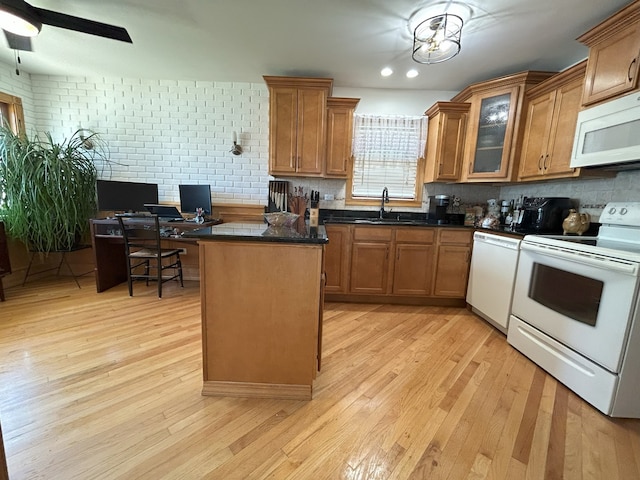 kitchen with white appliances, a sink, dark countertops, light wood-style flooring, and brown cabinets