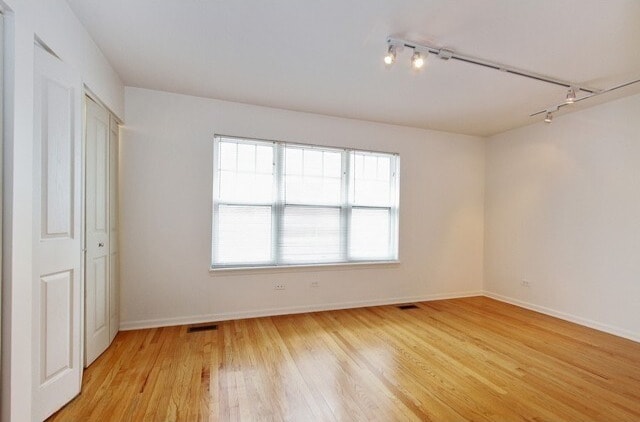 unfurnished bedroom with track lighting, light wood-style floors, baseboards, and visible vents