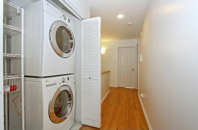 laundry room featuring baseboards, stacked washer / drying machine, light wood finished floors, and laundry area