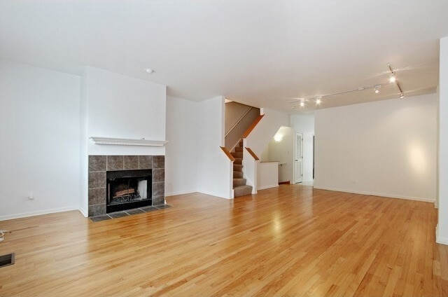 unfurnished living room featuring visible vents, a tiled fireplace, track lighting, stairs, and light wood-style flooring