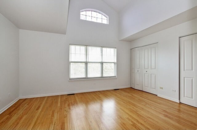 unfurnished bedroom featuring light wood finished floors, high vaulted ceiling, two closets, baseboards, and visible vents