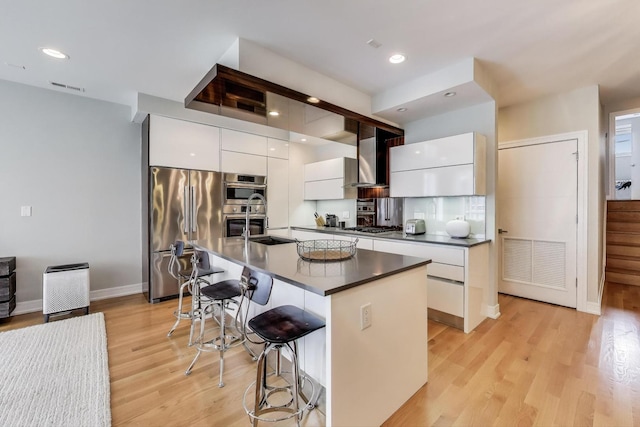 kitchen with modern cabinets, a kitchen breakfast bar, dark countertops, white cabinets, and appliances with stainless steel finishes