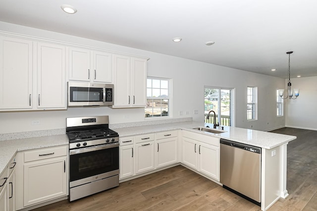 kitchen with white cabinets, appliances with stainless steel finishes, a sink, a chandelier, and a peninsula