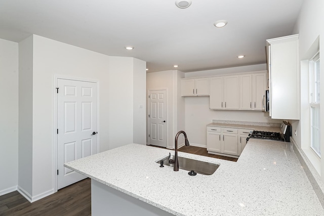 kitchen featuring light stone countertops, stove, a sink, white cabinets, and a peninsula
