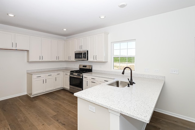 kitchen featuring dark wood-style flooring, a sink, stainless steel appliances, white cabinetry, and a peninsula