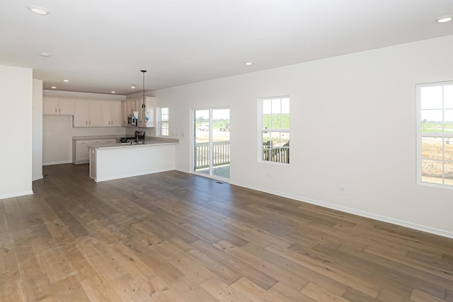 unfurnished living room featuring baseboards, recessed lighting, hardwood / wood-style floors, and a wealth of natural light
