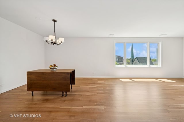 empty room with a chandelier, light wood-type flooring, and baseboards